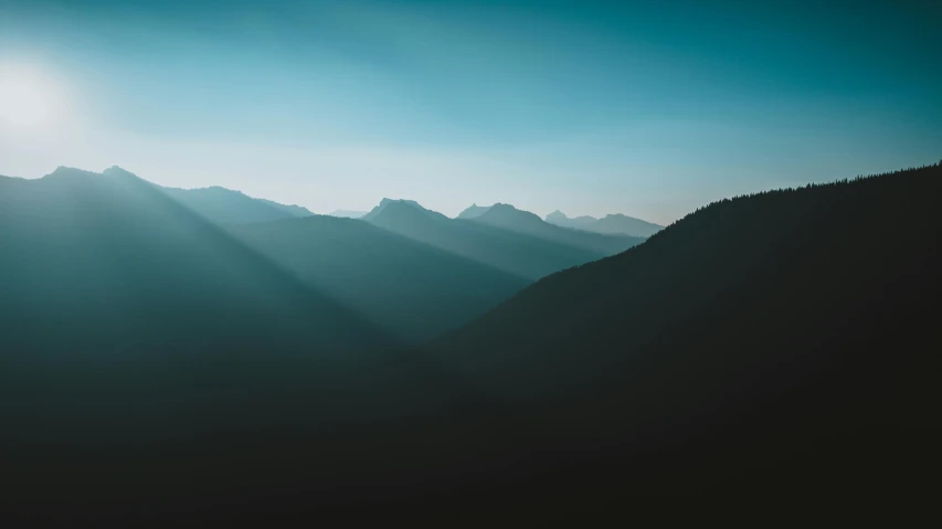 mountains are silhouetted against the bright blue sky with sun streaming through