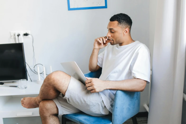 a person in shorts and a white shirt sitting in a chair with his feet on his desk