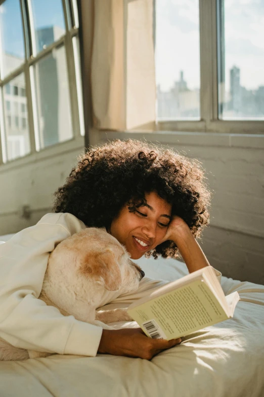 a beautiful woman laying in bed holding a book