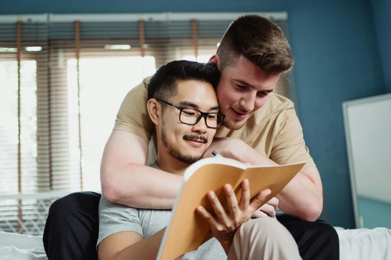 two men reading a book together in a bed room