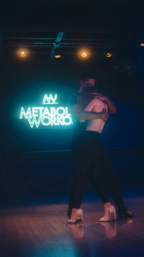 two people dancing a salsa in front of an illuminated sign