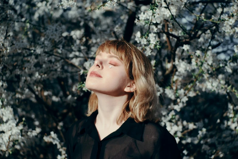 a woman looks to her left with eyes closed standing in front of a tree