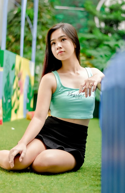 a beautiful young lady in a green top sitting on the grass