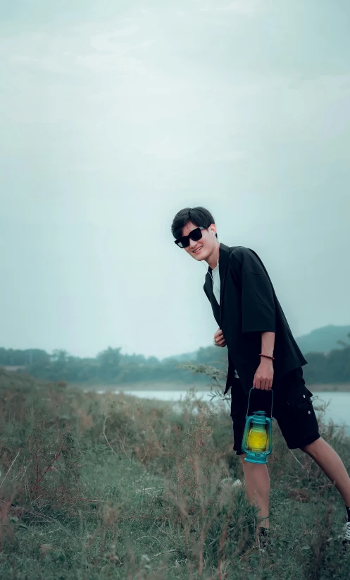 a man wearing sunglasses and holding a bucket standing on a grassy hillside