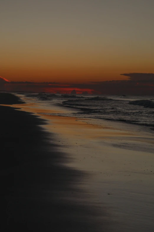 the sun is setting on a beach with the ocean in the foreground