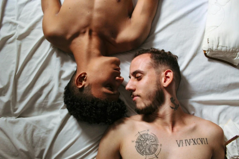 a man laying on his stomach next to another man's face on a bed