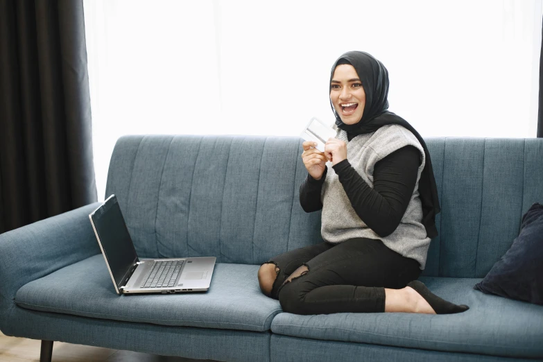 a young woman is smiling while sitting on the couch with a laptop