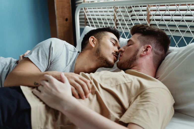 two guys laying in bed and kissing each other