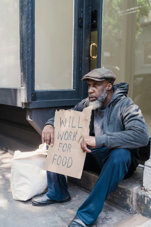 a homeless man sitting on the steps holding a sign that says will work for food