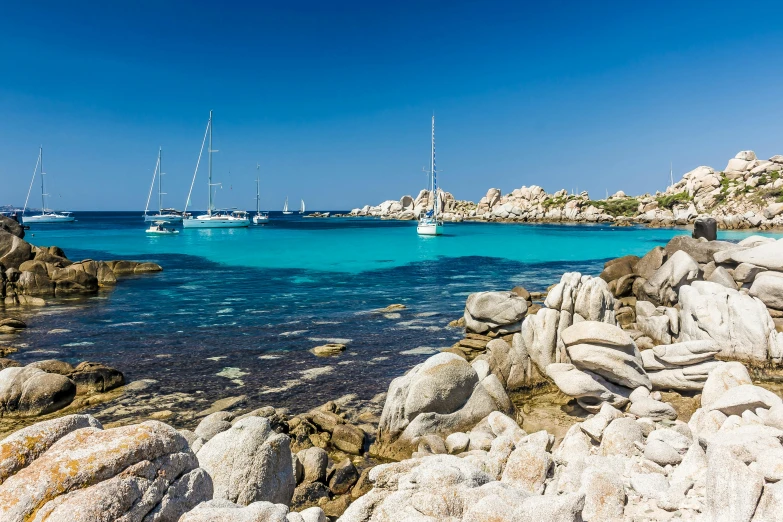 the rocks in the water are clear blue and there is a couple boats on the background