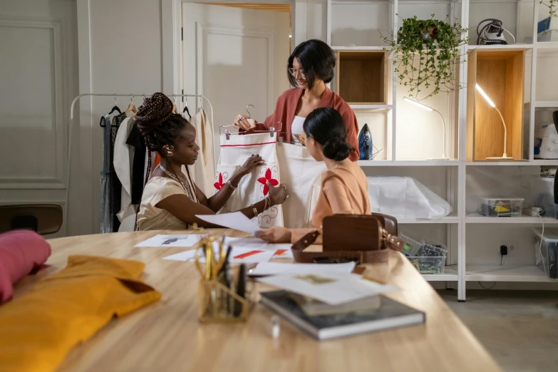 two women stand in front of a desk as another woman sits down and looks at the papers