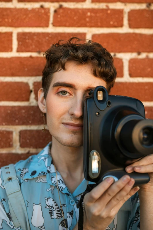 man in front of brick wall holding up a camera