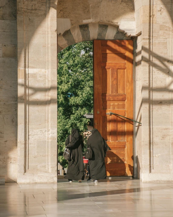 two people in dark black robes in front of a door