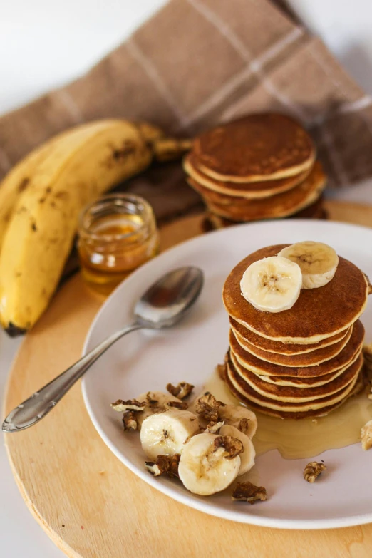 stack of pancakes with banana slices, maple syrup, and walnuts