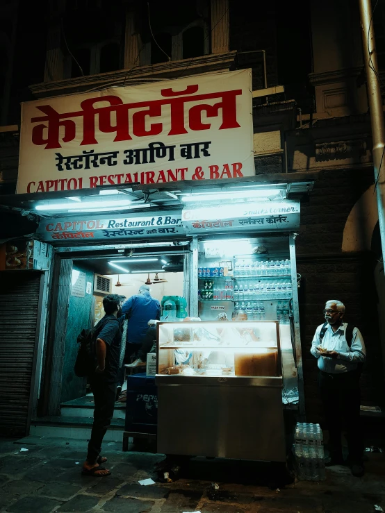 people stand outside of a restaurant with lights on