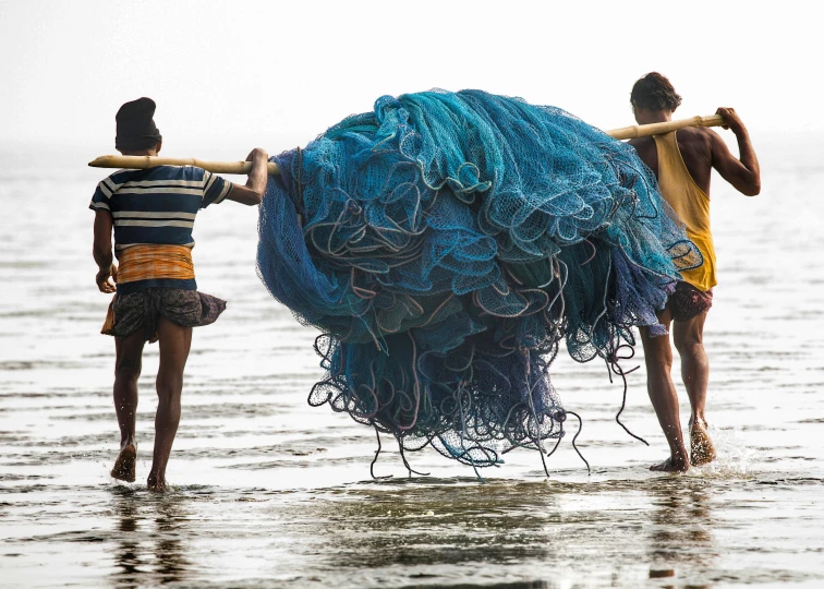 two boys are carrying a blue object on a rope