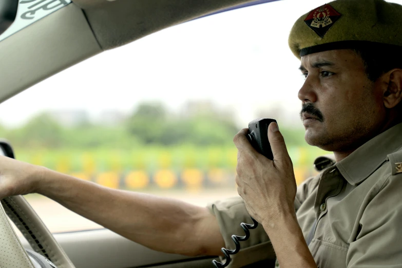 a uniformed man in the driver's seat of a vehicle on his cell phone