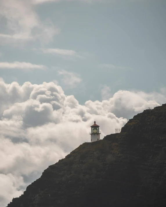 a hill with a lighthouse on top and clouds surrounding it