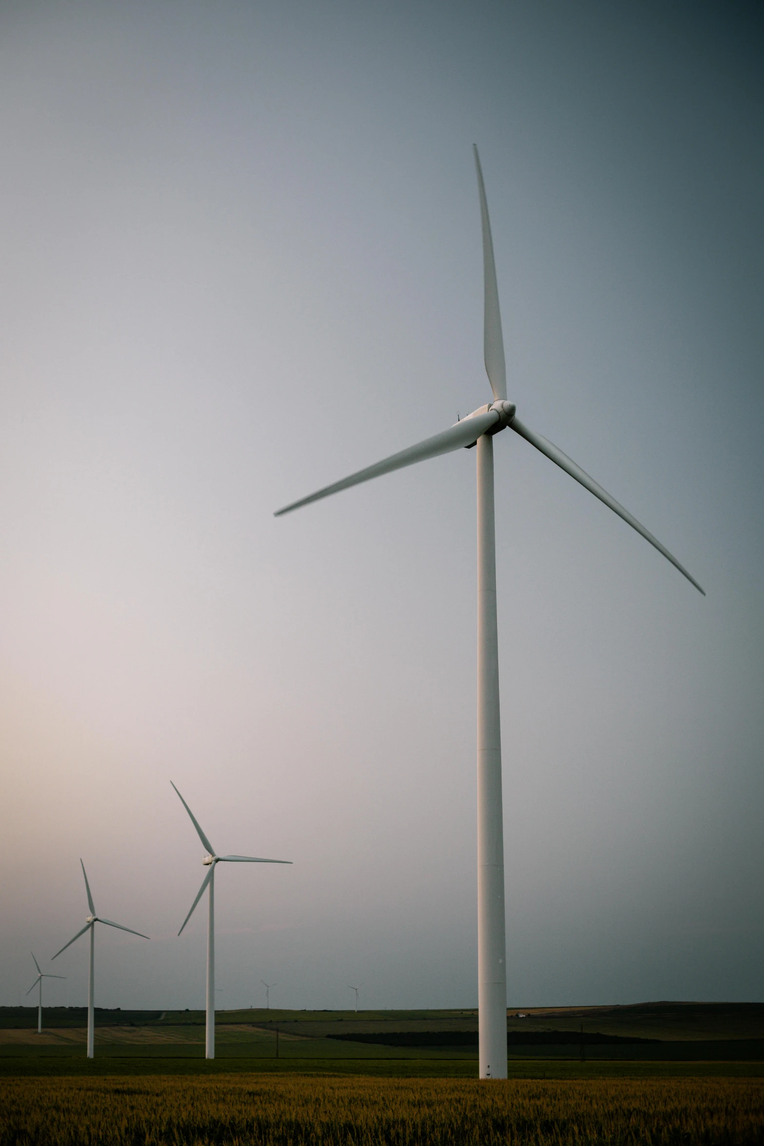 four windmills standing in a large field at dusk