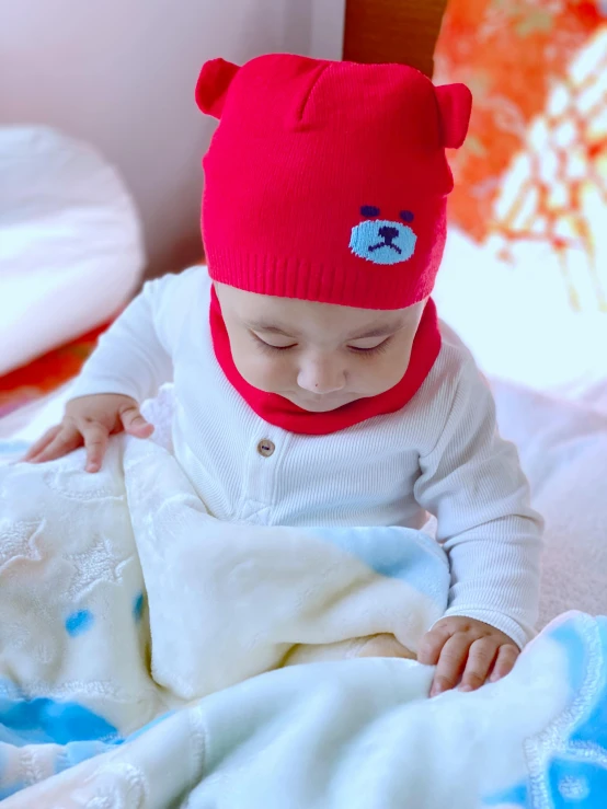 a baby wears a red bear hat on top of a blanket