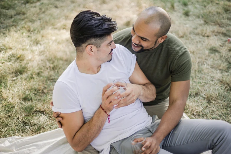 a man holding another mans chest while sitting in a field