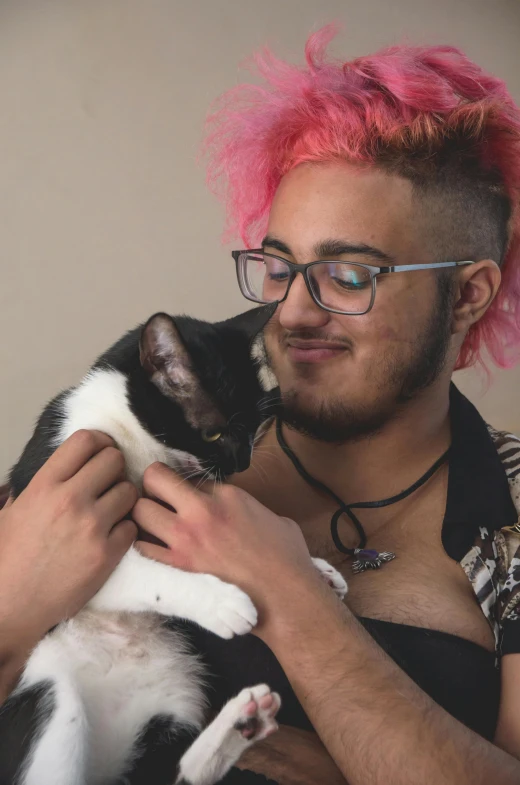 man with pink mohawk on his head with pink hair and glasses holding cat