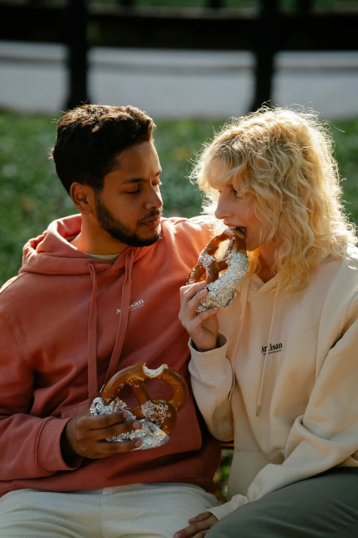 two people are eating food while sitting on the bench