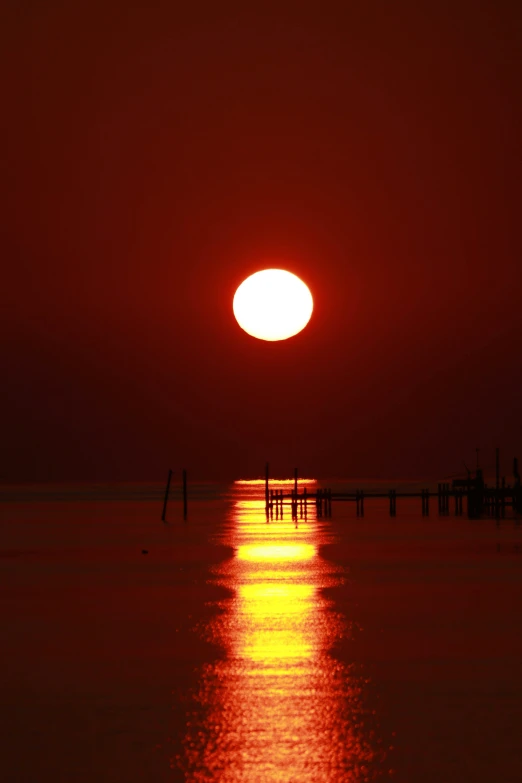 the sun rises over the water and creates a red orange sky