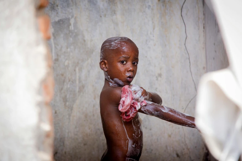 a young child covered in mud and foam, standing in an open doorway