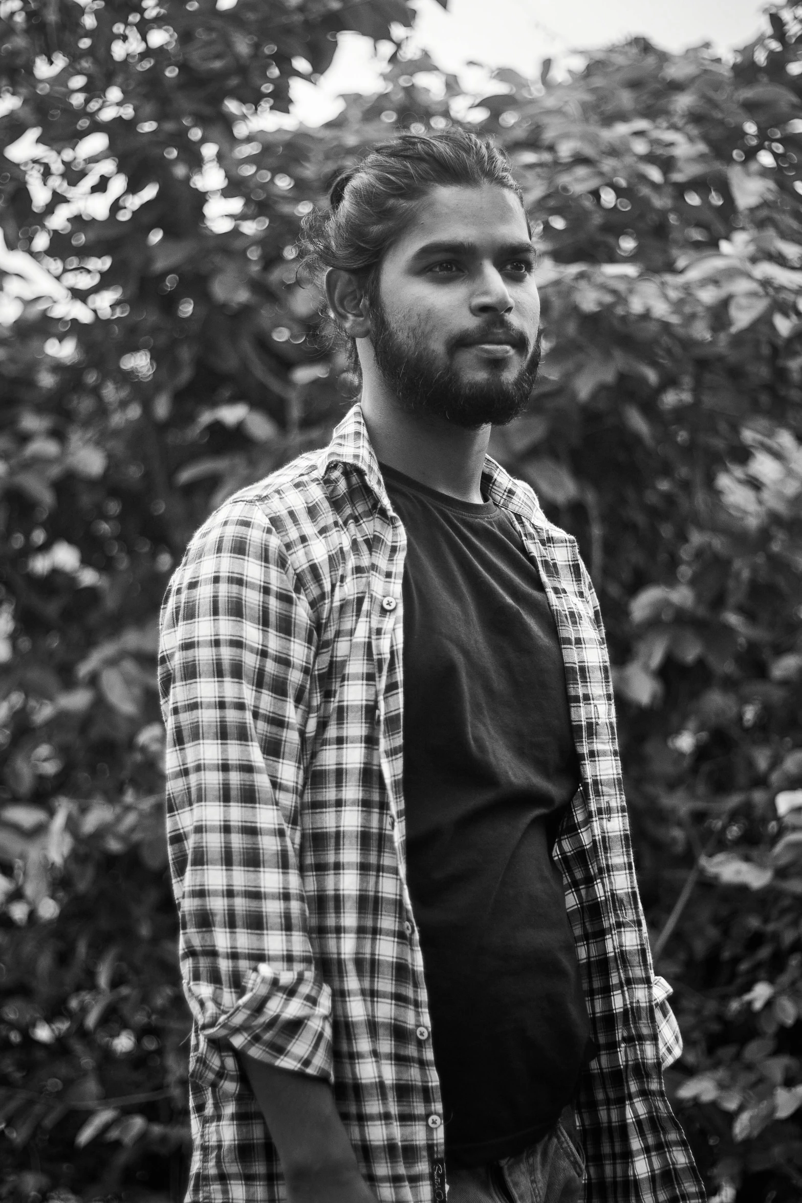 a man wearing plaid shirt standing in front of bushes