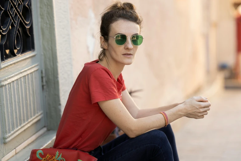 woman sitting on curb with green sunglasses wearing red shirt