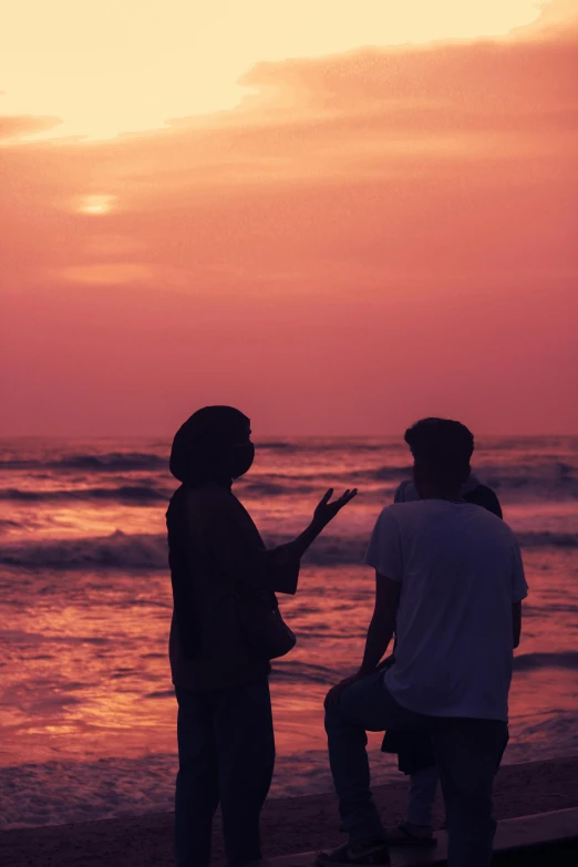 three people on a beach are silhouetted against the setting sun