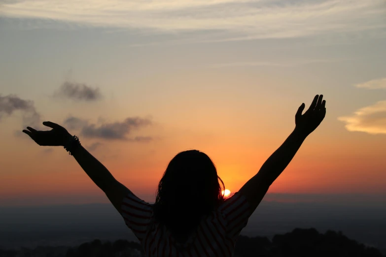 a woman is standing with her hands up with the sun rising in the background