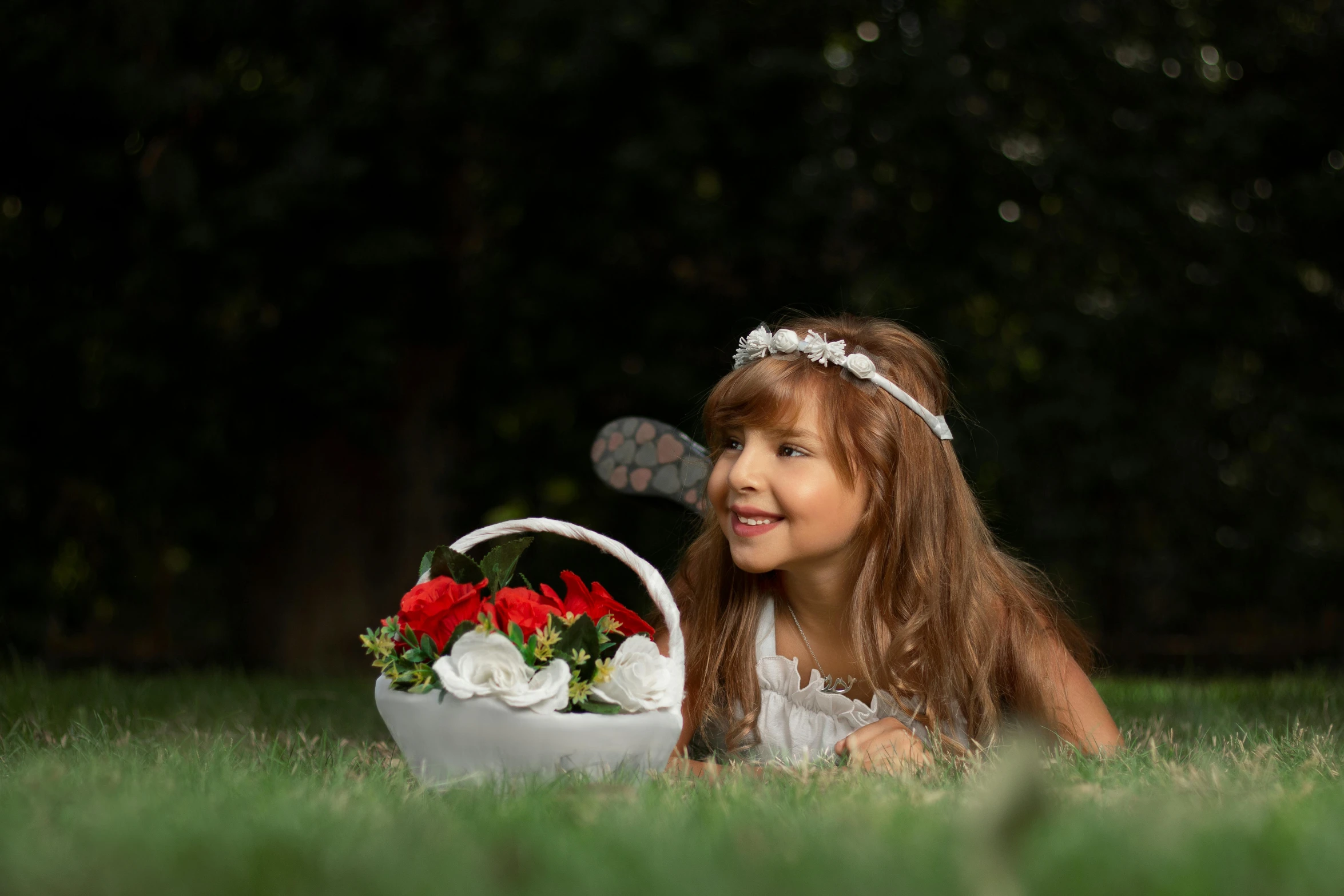 a small girl in white dress laying on grass with a basket of flowers