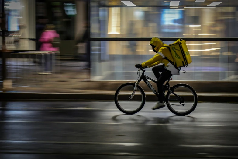 man with yellow jacket rides a bicycle in the rain