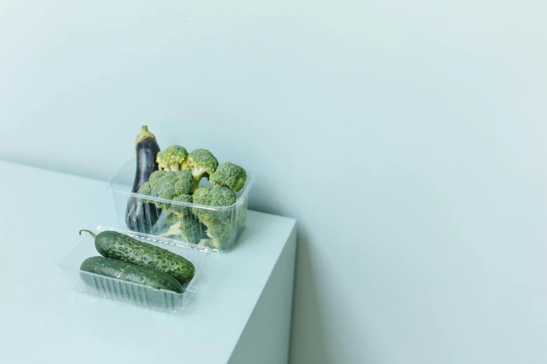 two plastic containers filled with cucumbers on a table