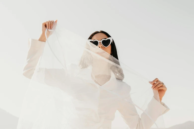 a woman wearing sunglasses holding a veil on her face