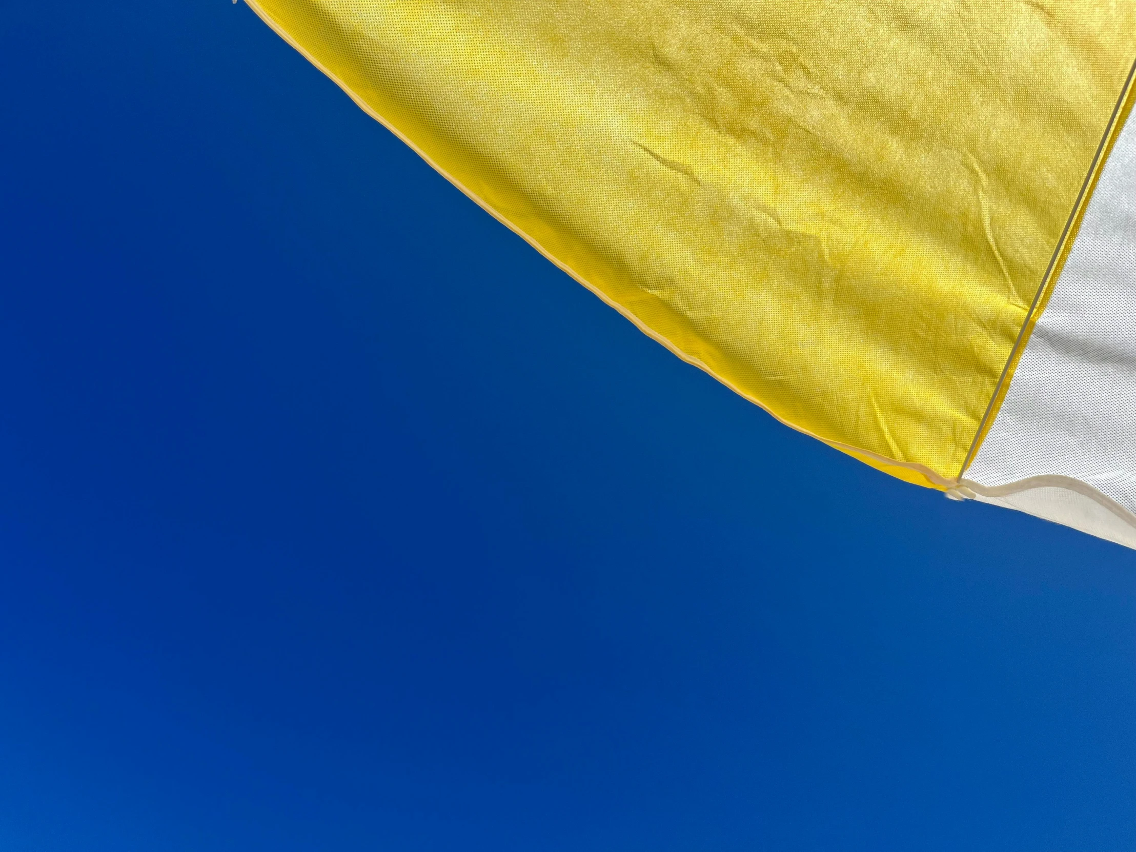 a yellow and white umbrella is open on a sunny day