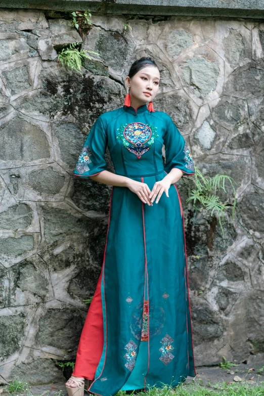 a woman wearing a blue dress stands near a stone wall