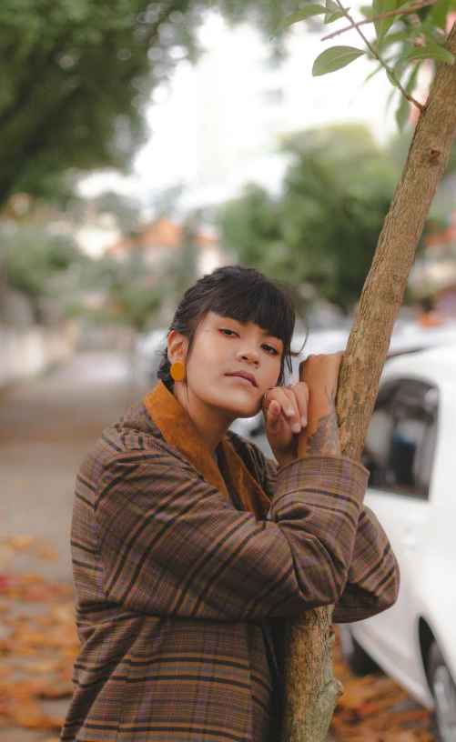 young asian girl leaning on tree holding cell phone