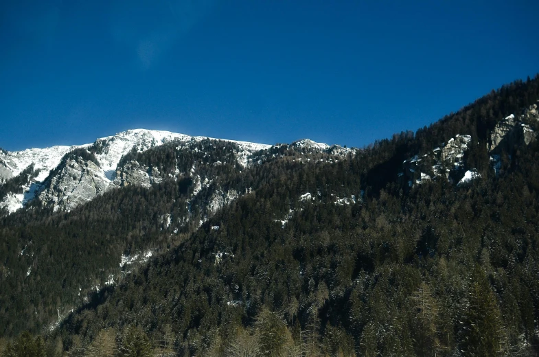 a mountain with trees in the foreground and a blue sky