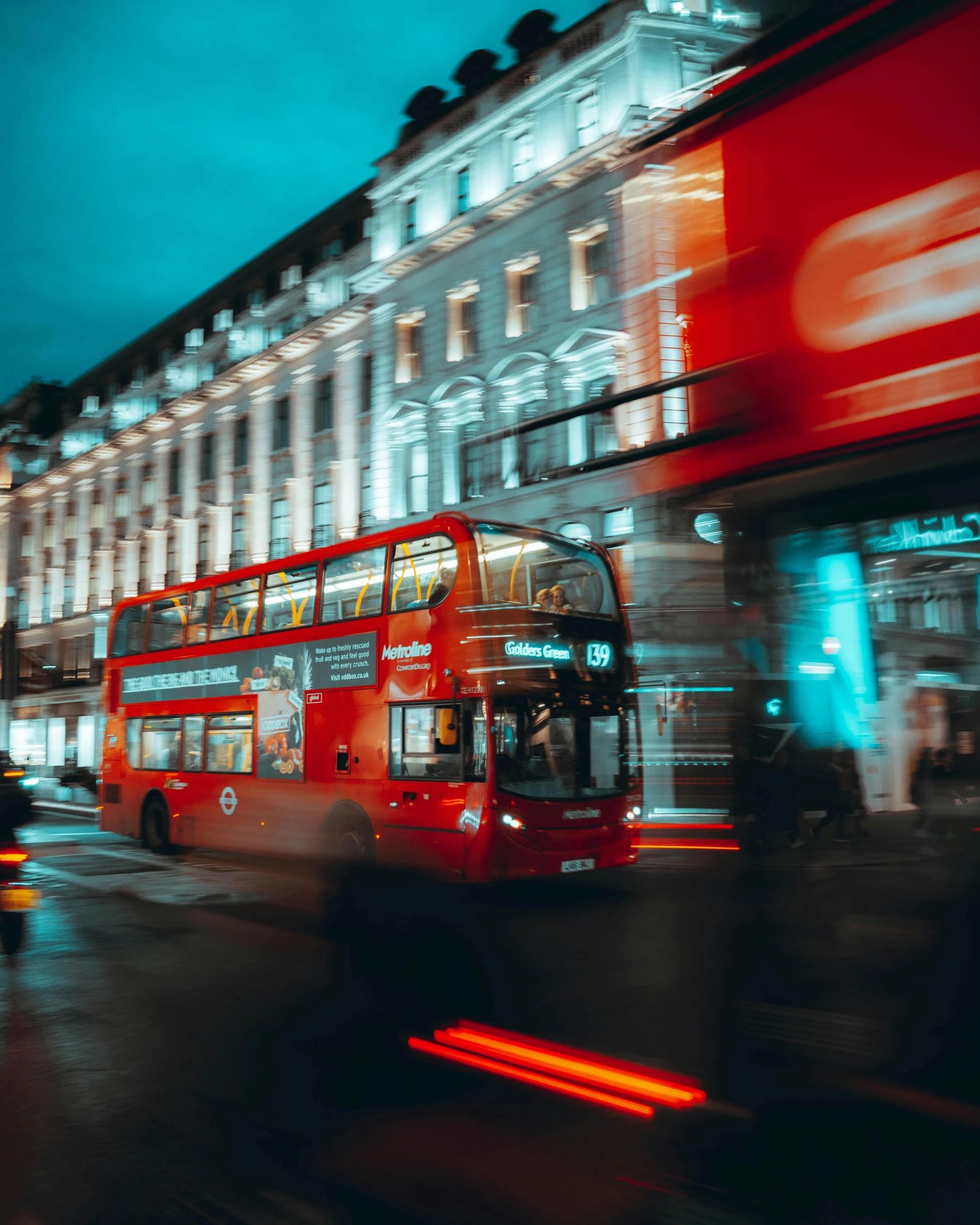 a double decker bus travels past the building and pedestrians