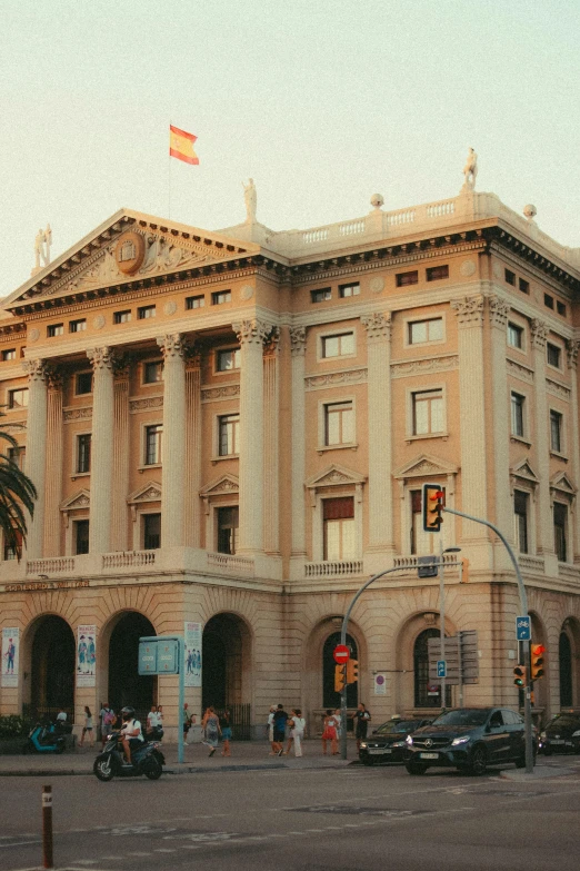 a large tan building with people walking on the sidewalk