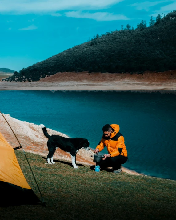 a man in yellow is kneeling by a tent with a black dog