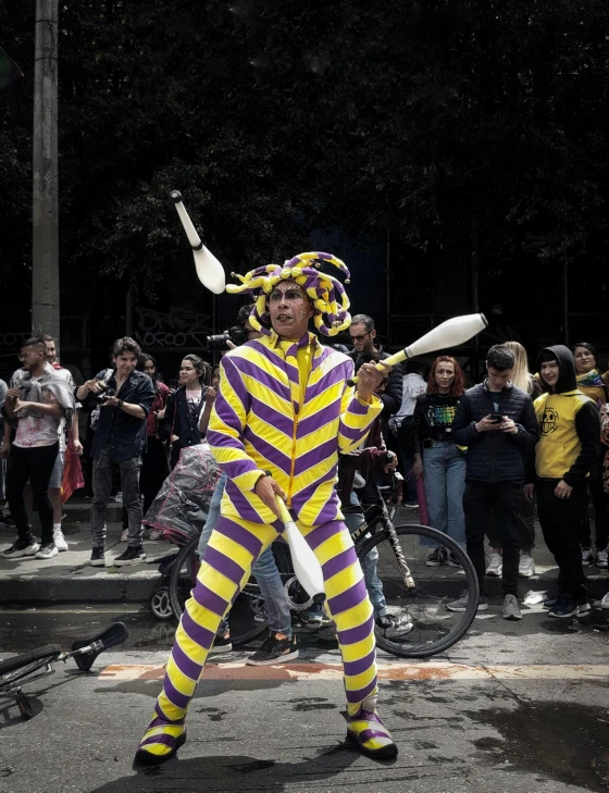 man dressed as a clown with a group of people on side of street