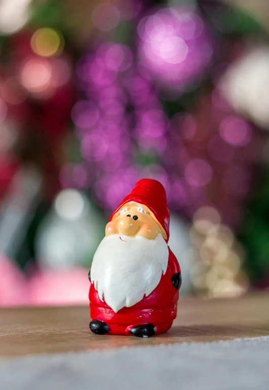 small santa claus figurine sitting on a table next to a christmas tree