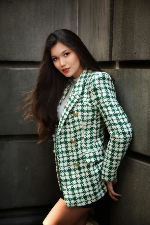 a woman is leaning against a wall wearing a green and white suit