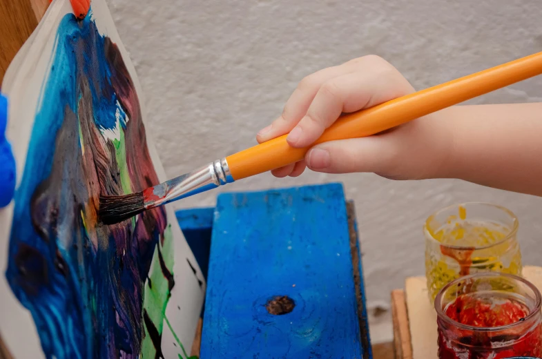 hand using paintbrush to create art on canvas
