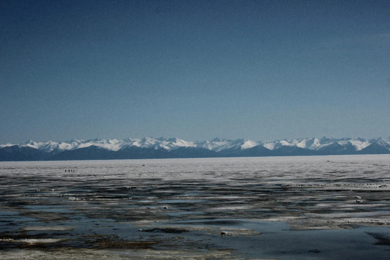 snowy mountains stand behind a calm ocean and sky