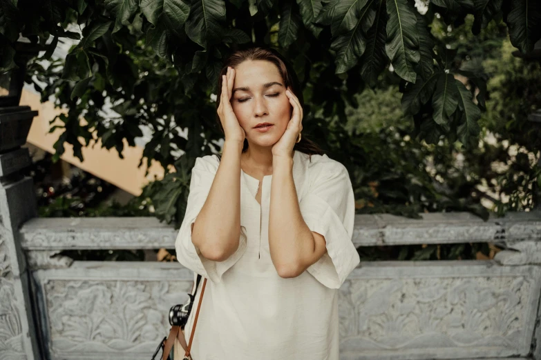 a woman with her hand on her face next to a fence